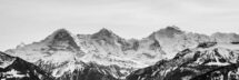 Black and white photo capturing majestic, snow-capped mountains in a serene winter landscape.
